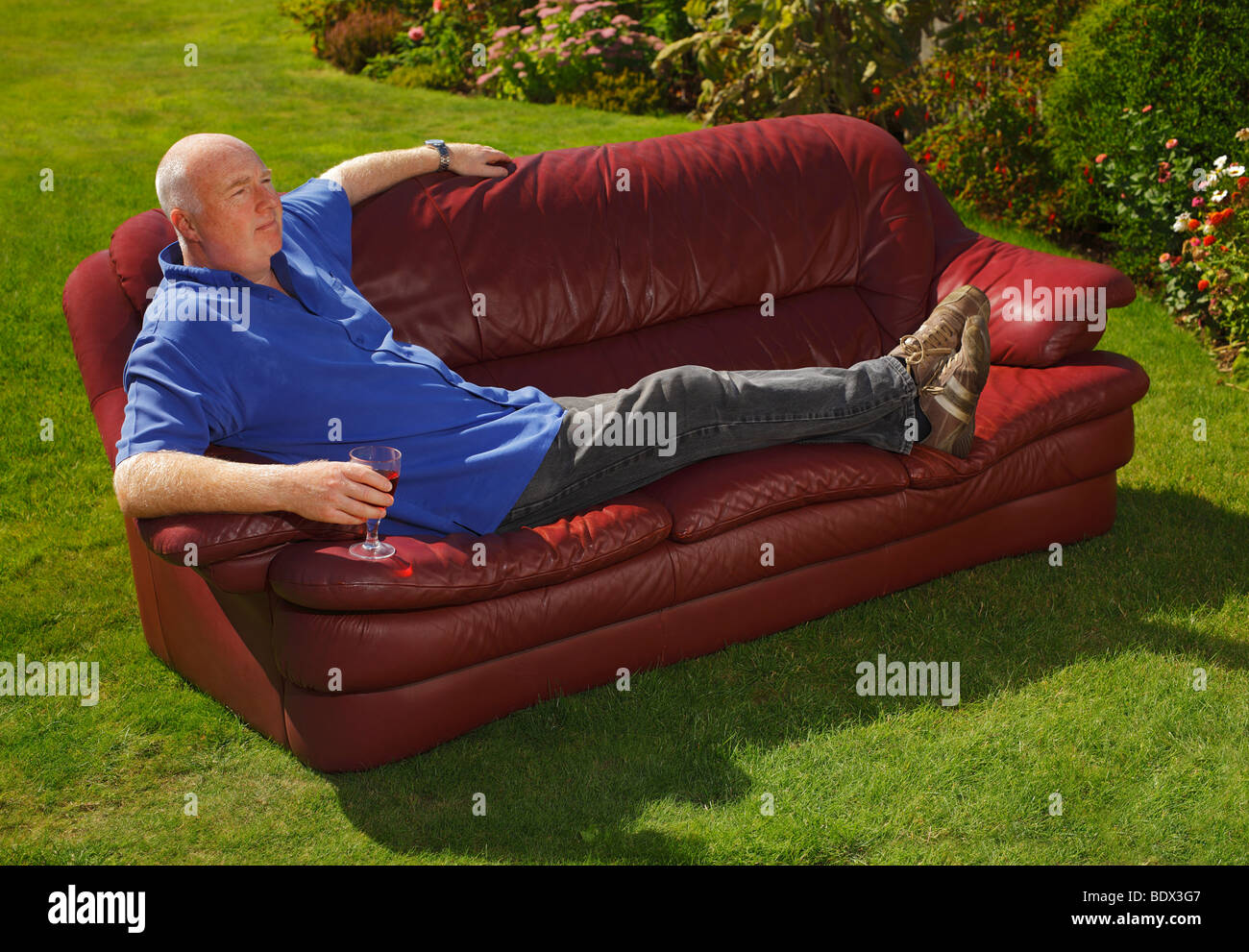 Uomo seduto in giardino su un divano con un bicchiere di vino. Foto Stock