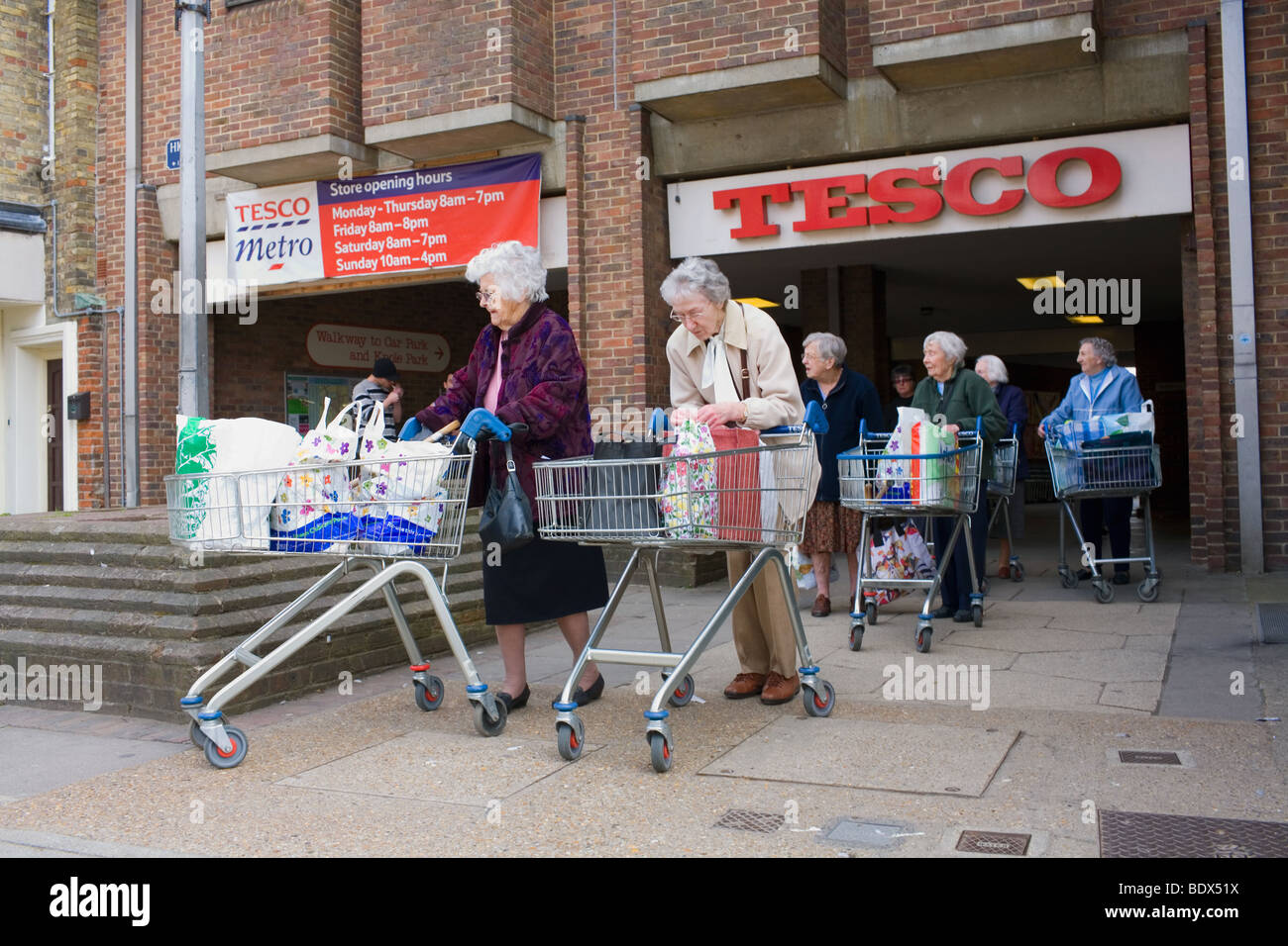 Una linea di donne anziane lasciare il supermercato Tesco con il loro carrello della spesa. Foto Stock