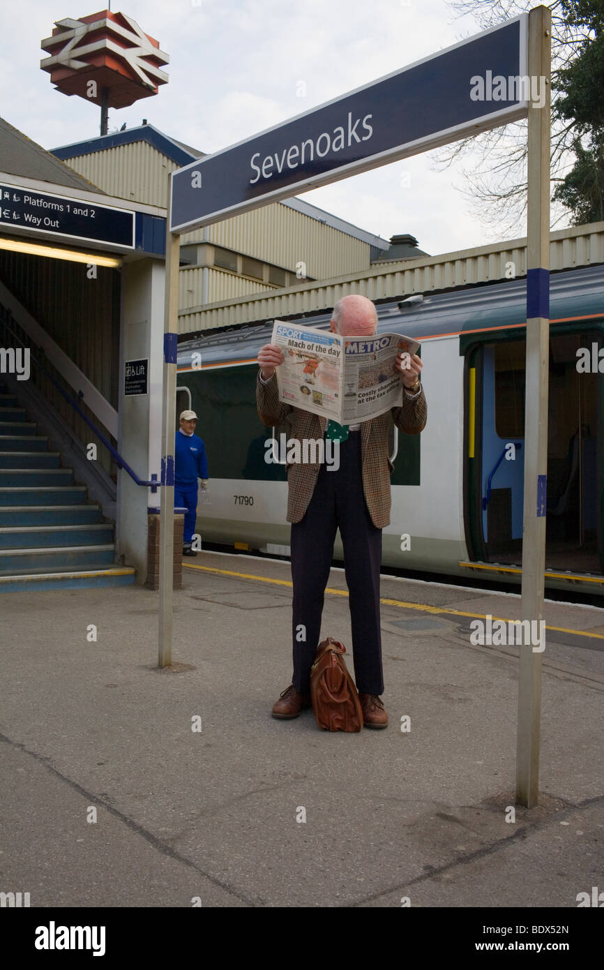 Un uomo anziano con povera vista legge un giornale mentre in attesa di una mattina eatly treno. Foto Stock