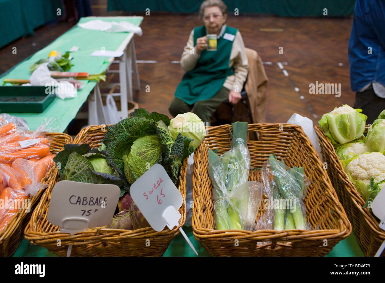 Un anziano volontario femmina vende verdure a un mercato di un paese in Sevenoaks town hall. Foto Stock