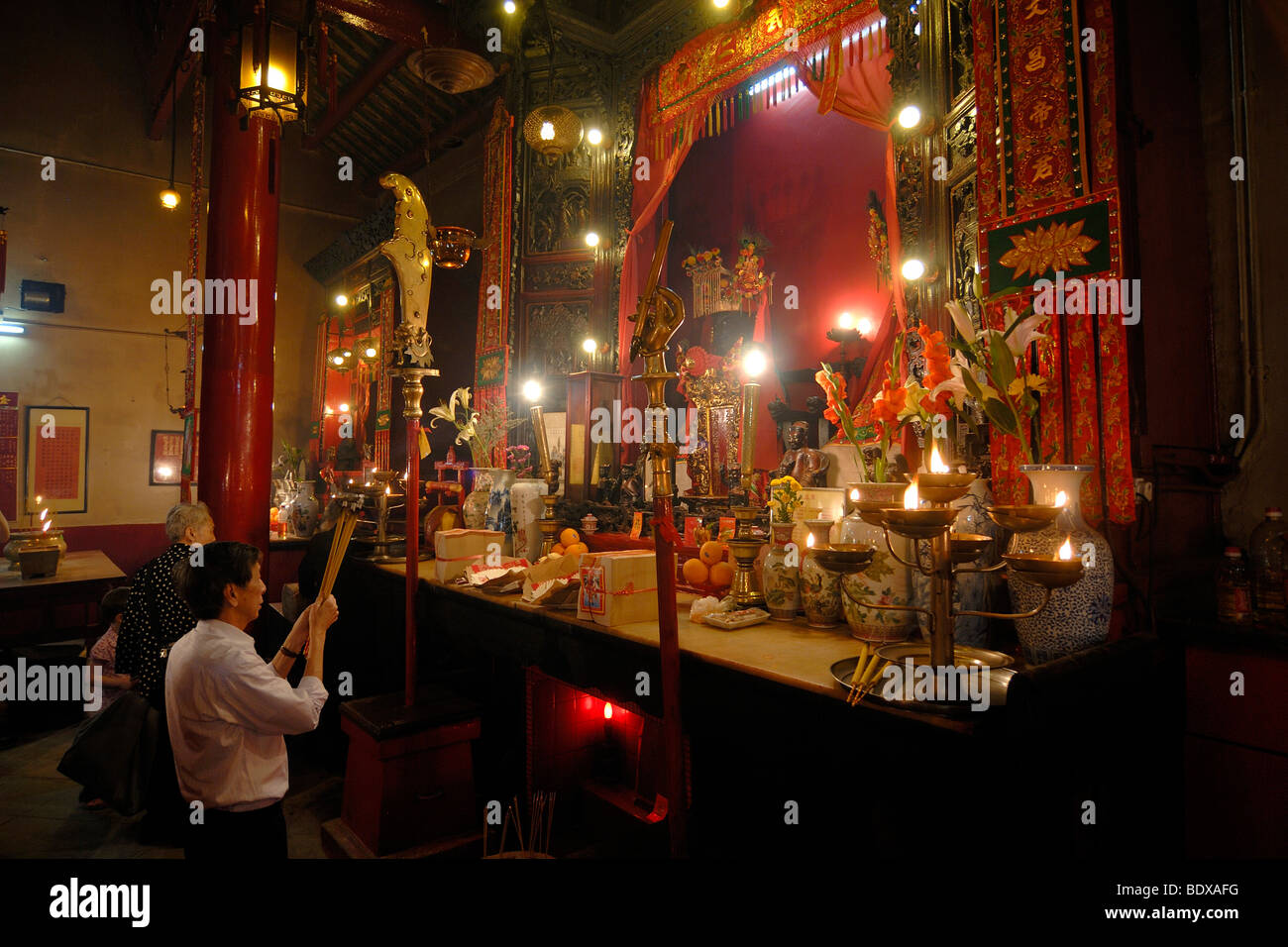 Uomo e donna che prega con bastoncini di incenso, fumo di sacrificio, di fronte a un cinese altare buddista con candele accese e speciali Foto Stock