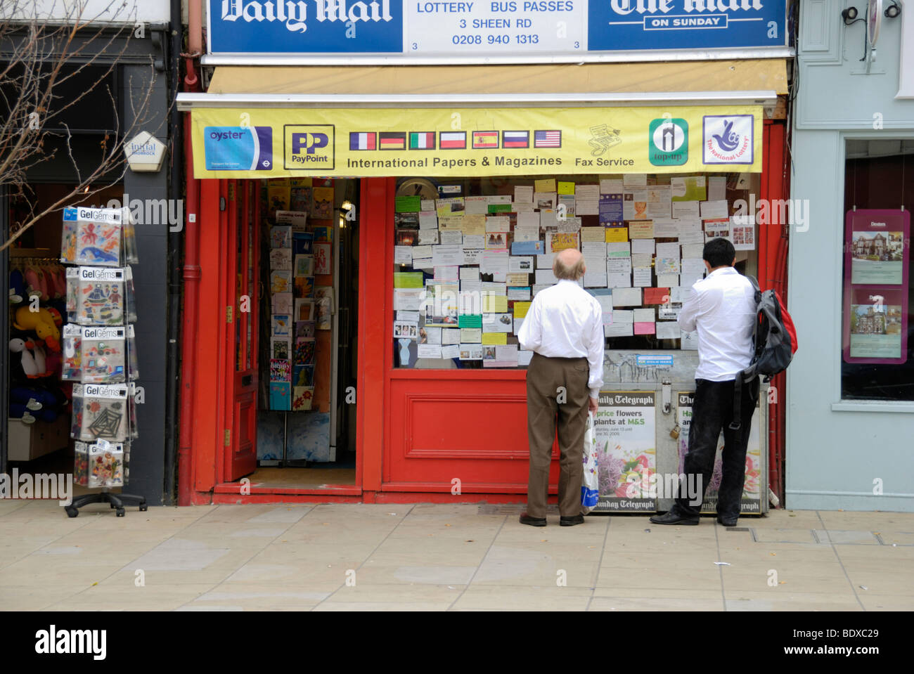 Due uomini guardando gli annunci pubblicitari in una edicola Negozio finestra, London, England, Regno Unito Foto Stock