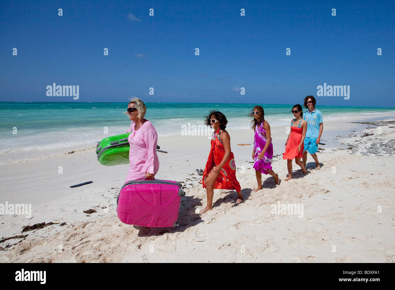 Madre in vacanza che porta le valigie per la sua propria famiglia sulla spiaggia Foto Stock