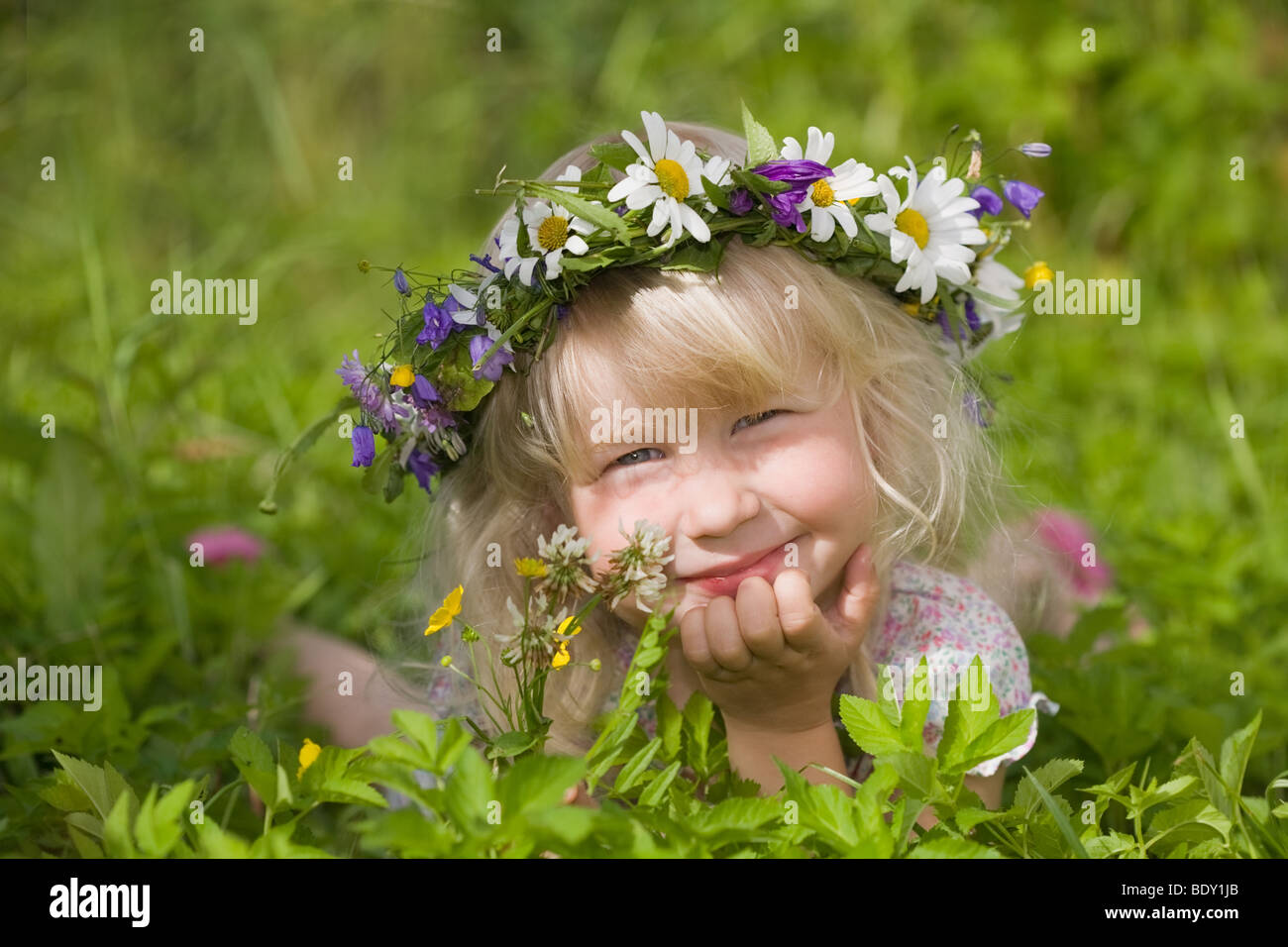 Felice bambina in ghirlanda di fiori che giace sul verde prato Foto Stock