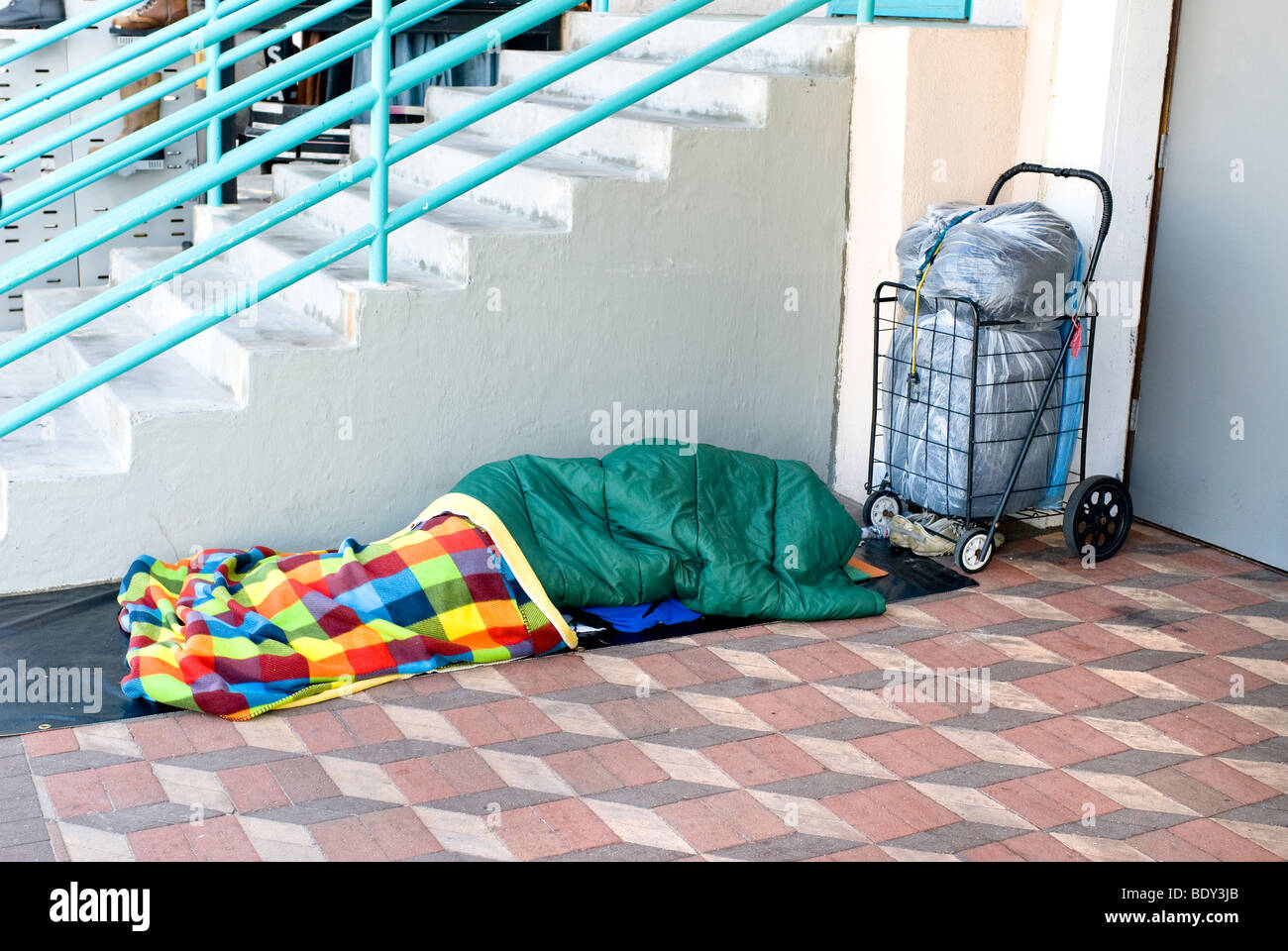 Una persona senza dimora dormono lungo un marciapiede di mattoni. Foto Stock