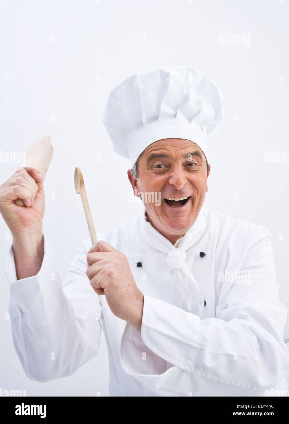 Lo Chef indossando un chef hat tenendo un cucchiaio di legno e un matterello nelle sue mani Foto Stock