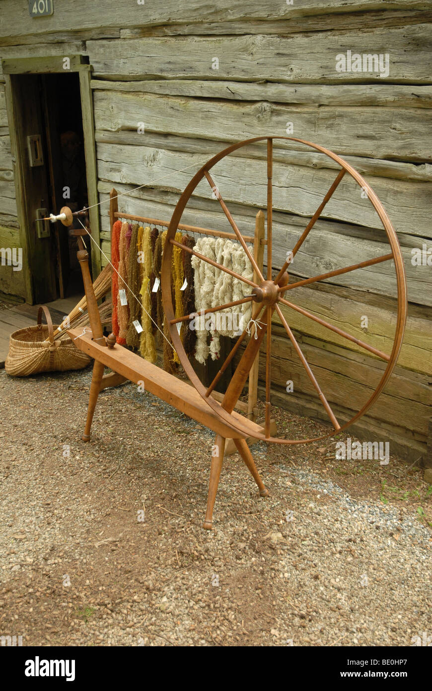 Una ruota di filatura si trova al di fuori di una vecchia cabina con filato. Foto Stock