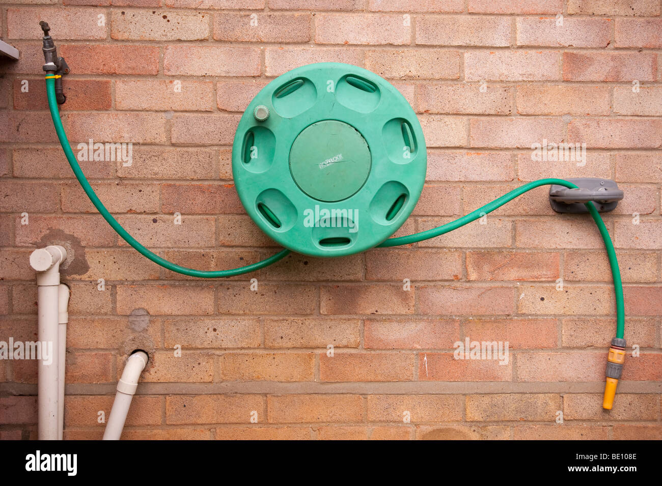 Un vento apribile fino a garden il tubo flessibile fissato ad una parete e collegato ad un rubinetto esterno nel Regno Unito Foto Stock