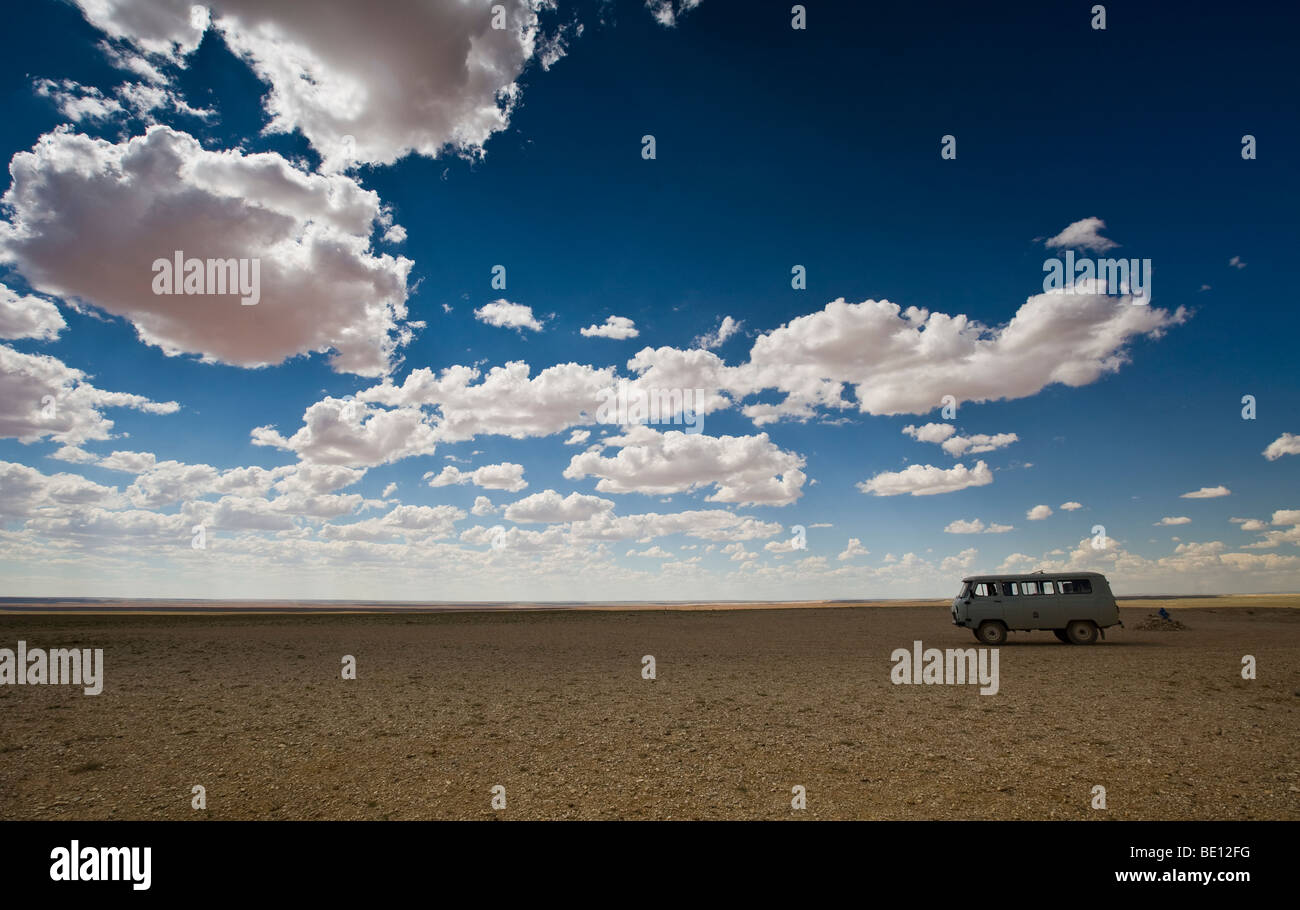 La jeep russa dell'era sovietica viaggia su distese piatte del deserto del Gobi con cielo blu e nuvole sullo sfondo Foto Stock