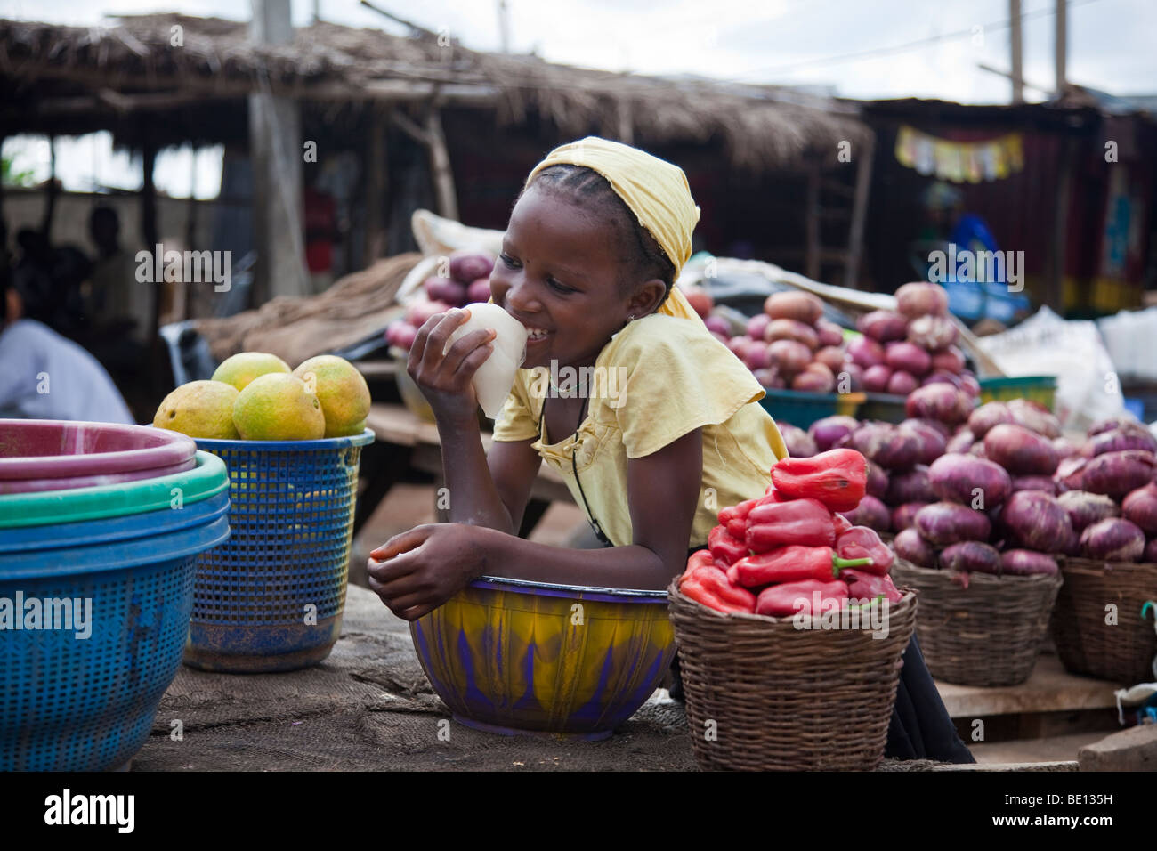 Una giovane ragazza Fulani bevande 'kunu' da un sacchetto di plastica, mentre manning la frutta e la verdura a tavola un mercato stradale in Nigeria. Foto Stock