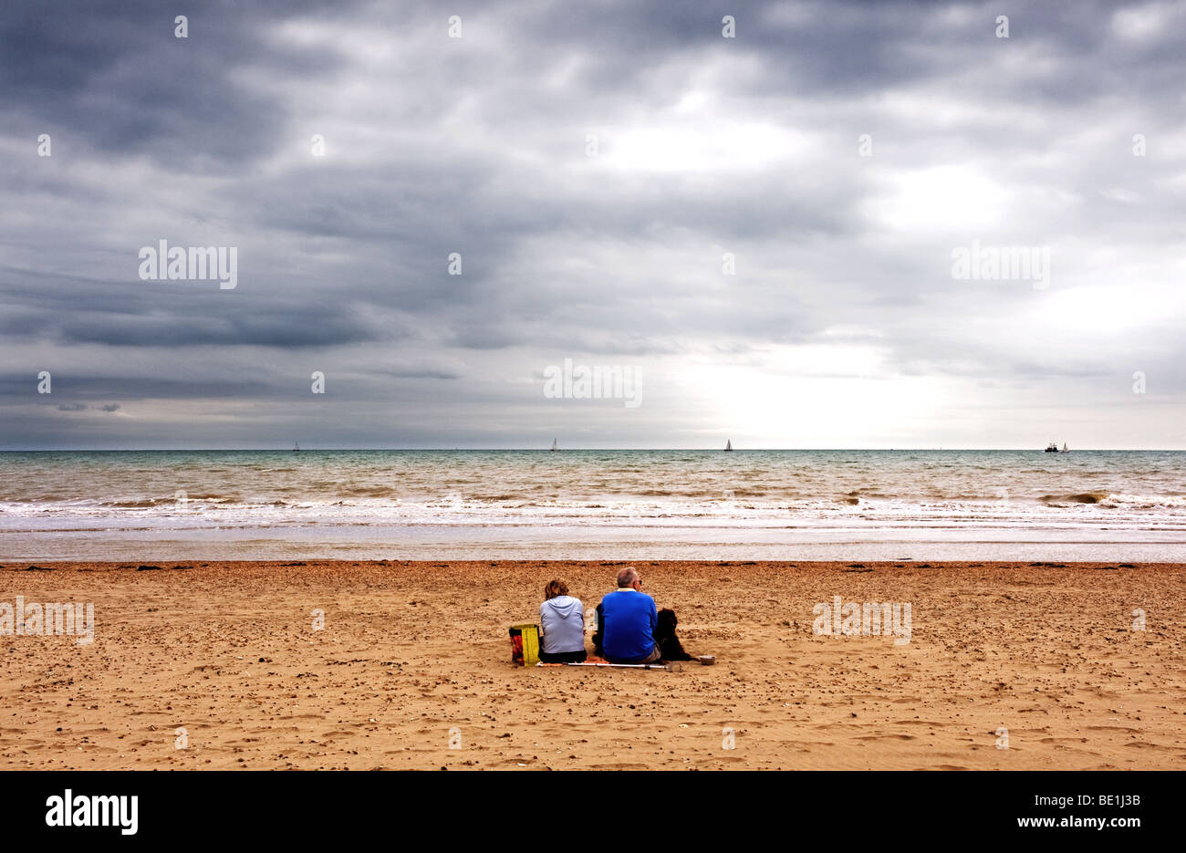 Un giovane seduto sulla spiaggia in una fredda giornata di Camber Sands in East Sussex. Foto Stock
