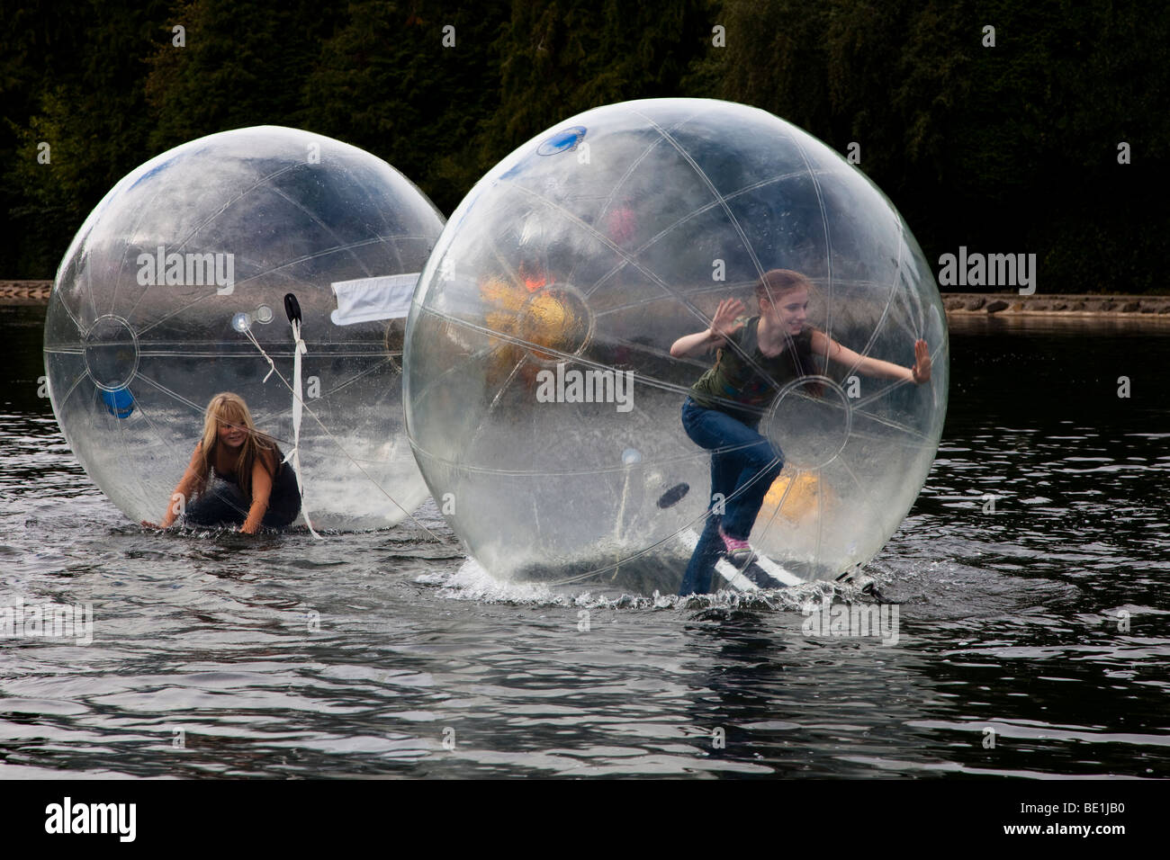 Due giovani ragazze a giocare all'interno di un bubblerunner attraverso il lago di pubblico a Rouken Glen Park, Glasgow, Regno Unito, Scozia Foto Stock