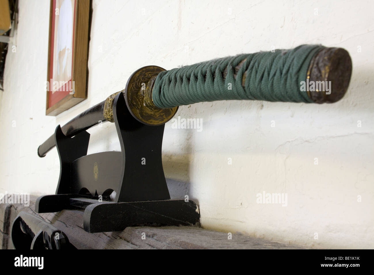 Unico giapponese refilato spada - katana in una kake conservato nel suo fodero (o saya) all'shomen, o parete anteriore del dojo. Anche il Kamiza o sede degli dèi. Una struttura in legno con un giapponese di sentire. La katana ha un aspetto caratteristico: una curva, snello, singola lama tagliente, circolare o quadrata, protezione e impugnatura lunga per ospitare due consegnato l'uso. Foto Stock