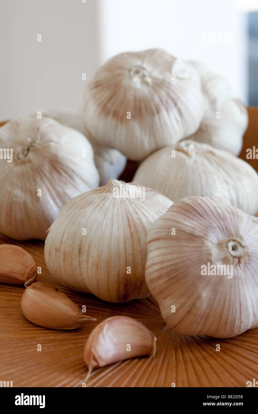 Close up di interi spicchi di aglio sul piatto di legno contro uno sfondo bianco. Verticale/formato ritratto. Foto Stock