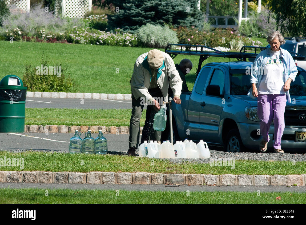 Un uomo e una donna di riempimento brocche di plastica con acqua fresca da un esterno di toccare il codolo. Foto Stock