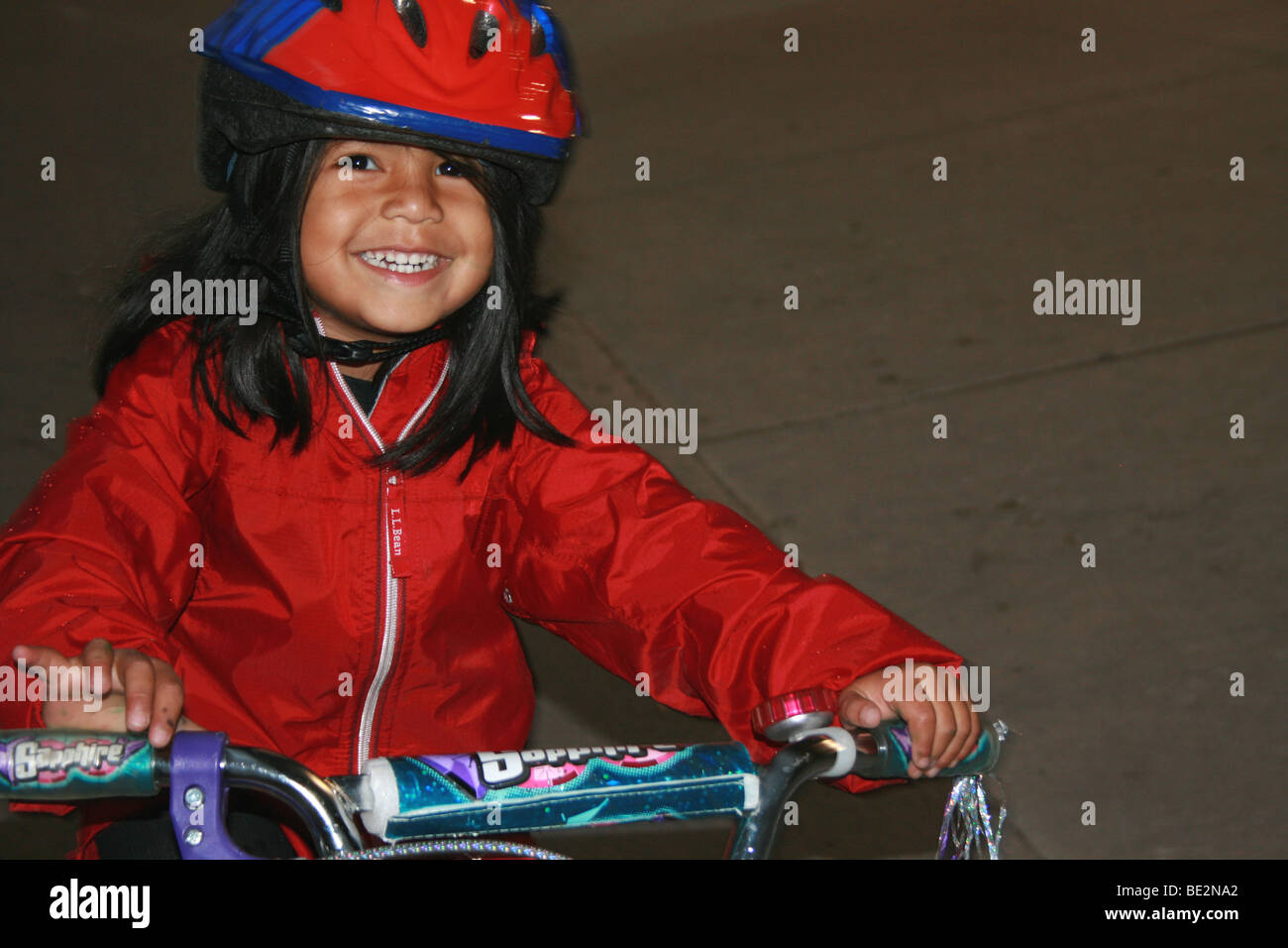 Tre anni di ragazza sorridente e passeggiate in bicicletta, indossa un casco Foto Stock