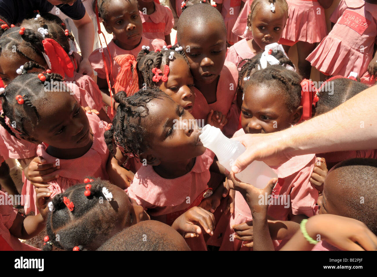 Gli scolari ad Haiti attendere per un drink di acqua pulita da un lavoratore di aiuto. Foto Stock
