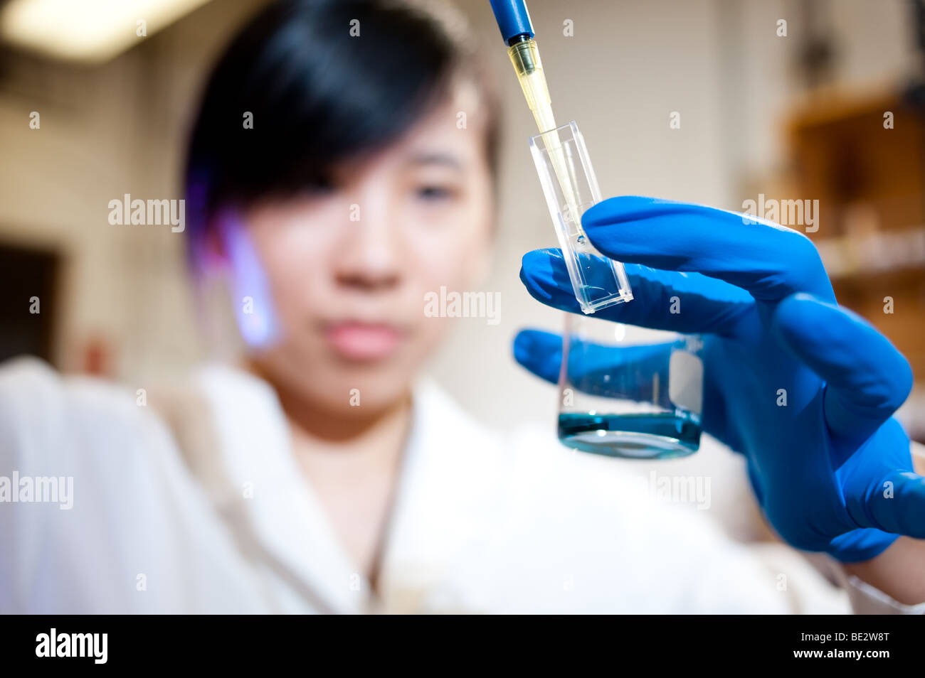 Science Student con pipeter in bianco camice, trasferimento di soluzioni al bicchiere Foto Stock