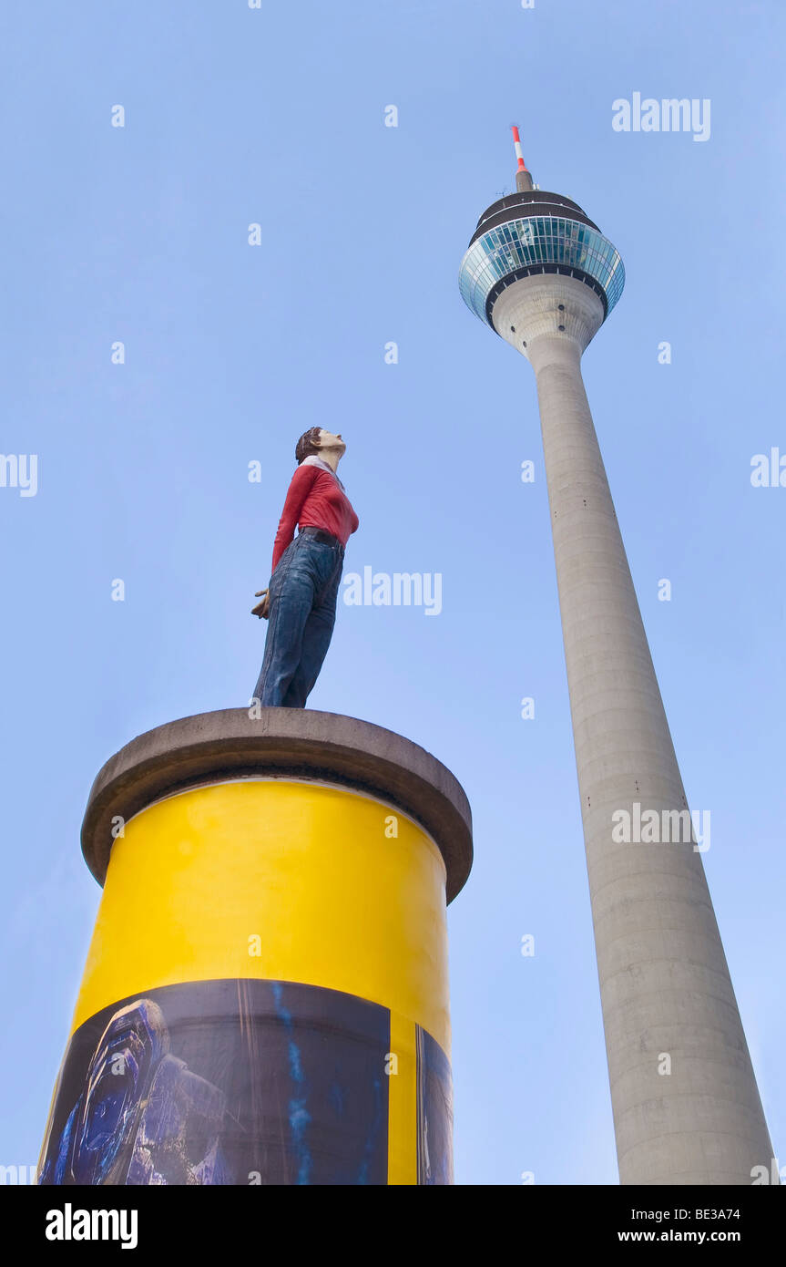 Colonna di pubblicità, la scultura di una donna che guarda verso l'alto, torre Rheinturm nel retro, Duesseldorf, nella Renania settentrionale-Vestfalia, Germania, Foto Stock