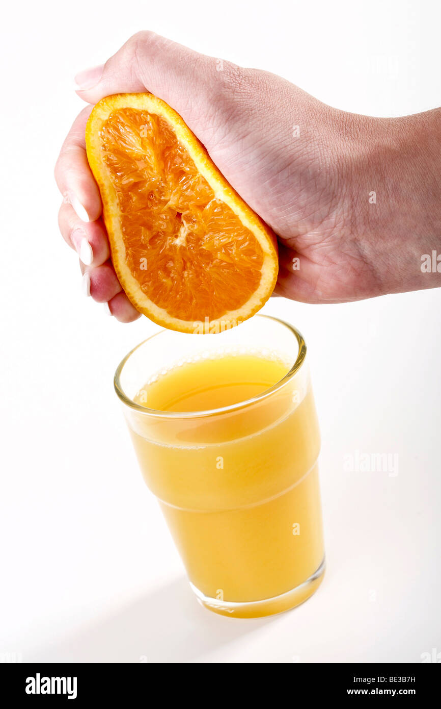 Spremitura a mano di colore arancione al di sopra di un bicchiere di succo di arancia Foto Stock