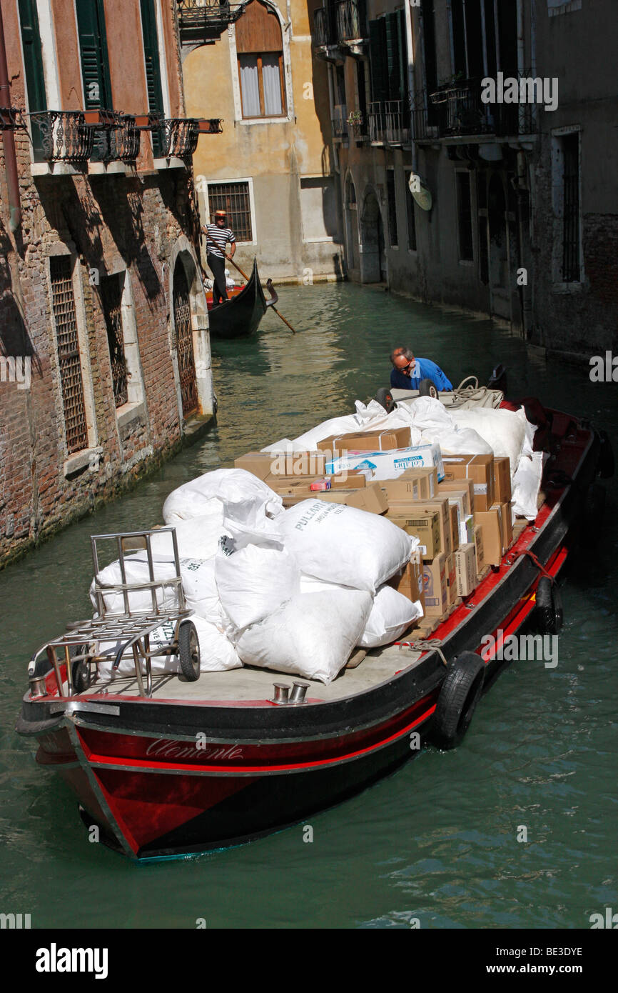 Barca di movimentazione di un carico di forniture lungo un canale di Venezia. Foto Stock