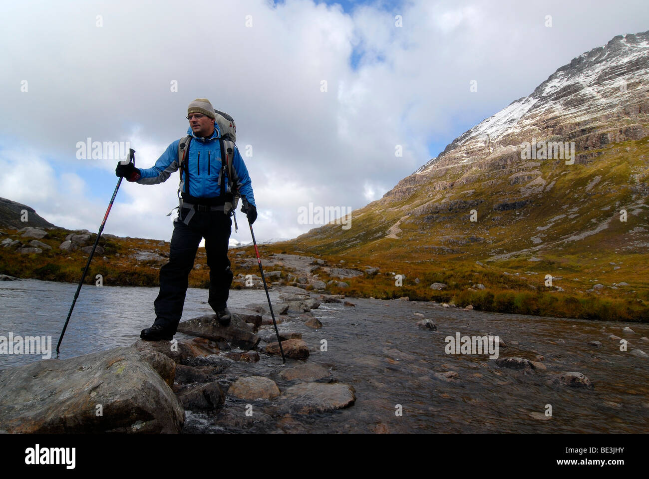 Escursionista con bastoncini da trekking e zainetto attraversare un fiume nelle montagne scozzesi, Highlands scozzesi, Stuca "Coro Dhuibh Beig Foto Stock