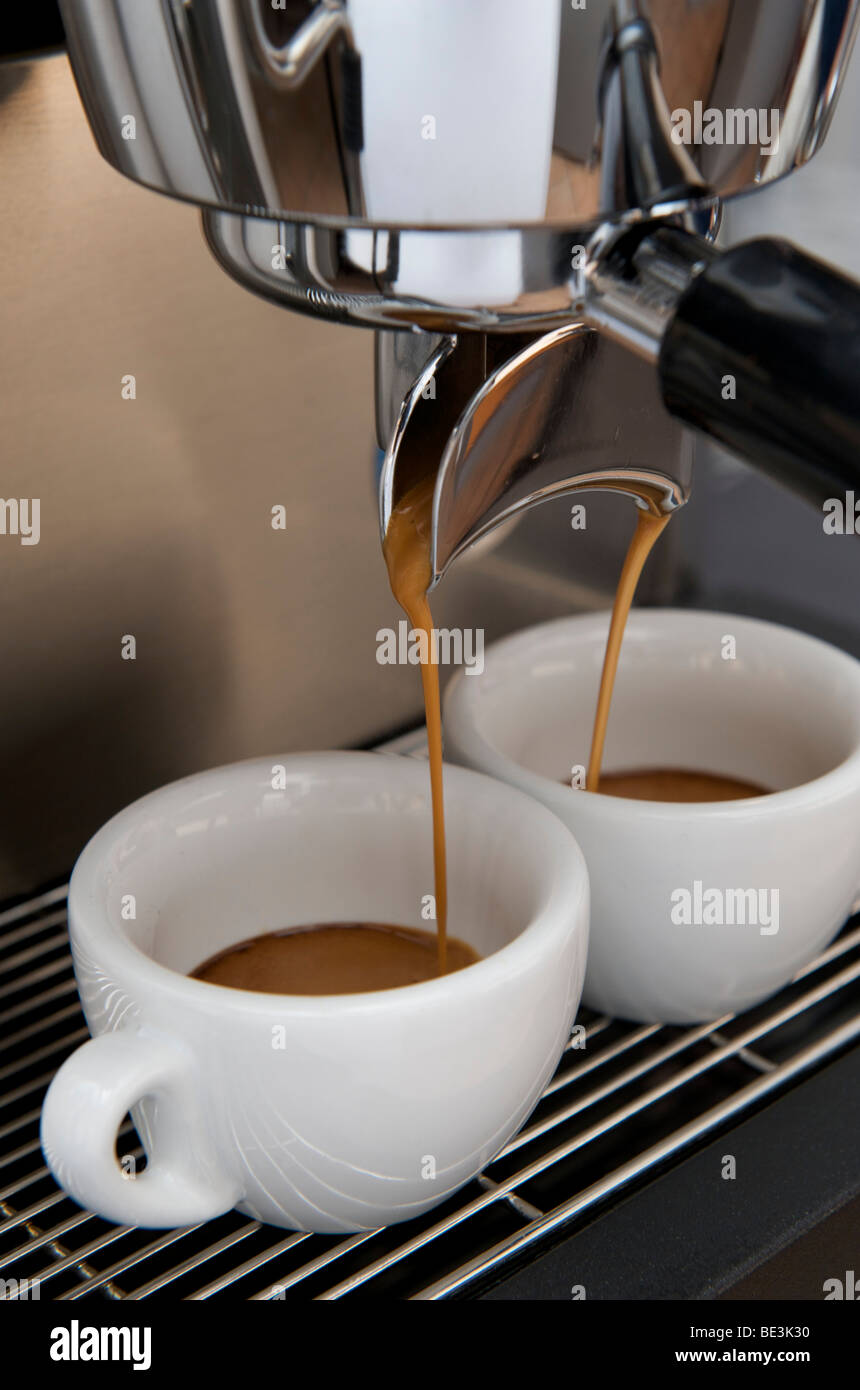 La preparazione professionale di espresso con una macchina espresso: il caffè espresso è che fluisce fuori del filtro nelle tazze da caffè Foto Stock