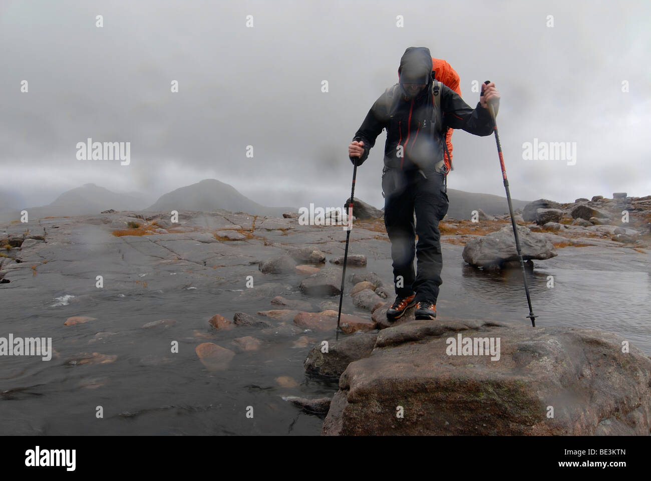 Hikerswith Escursionismo poli e e slicker attraversare un fiume nella pioggia scozzese, Highlands scozzesi, Liathach Torridon, Scozia, Foto Stock