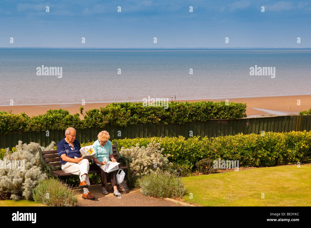 Due pensionati seduti su una panchina sul lungomare leggendo i quotidiani a Hunstanton , North Norfolk , Regno Unito Foto Stock