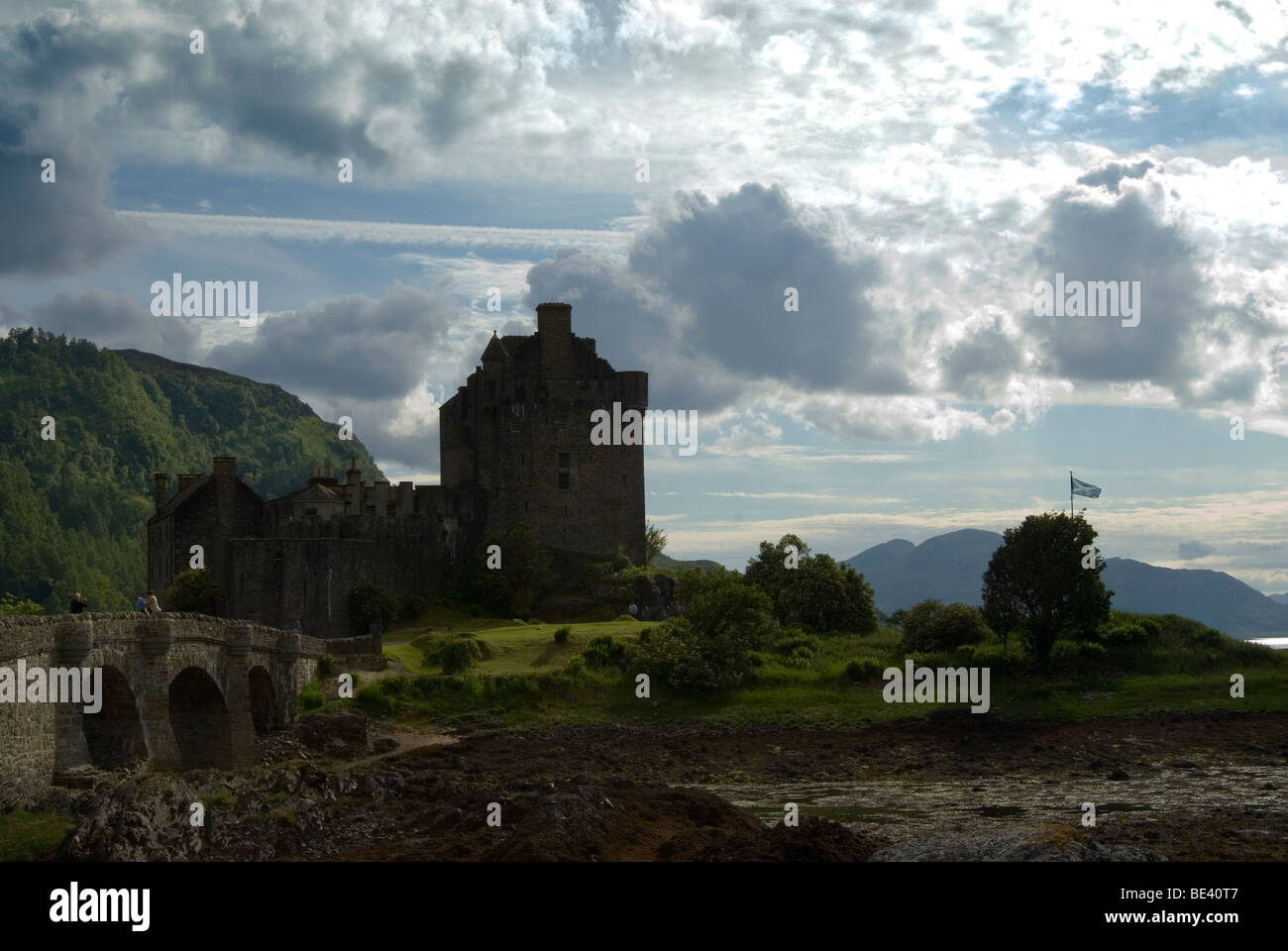 Eilean Donan Castle retroilluminato in una bella giornata con alcune nuvole il ponte del castello sulla sinistra e la bandiera della Scozia battenti Foto Stock