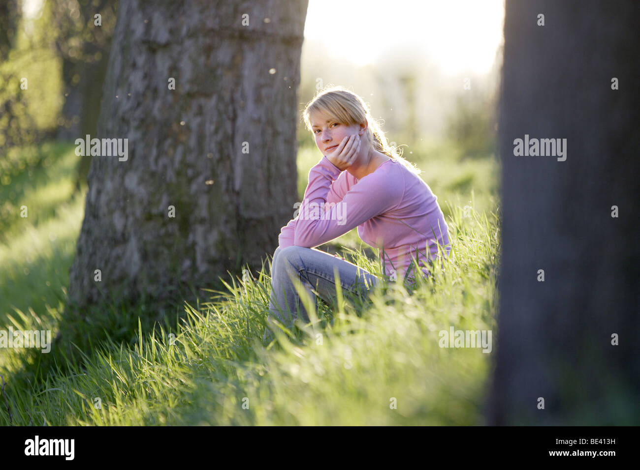 Junge Frau sitzt im Gras zwischen Baeumen Foto Stock
