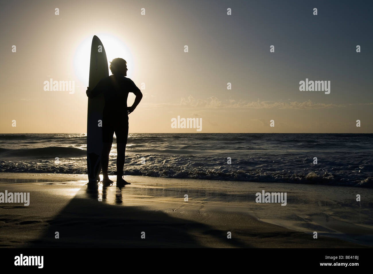 Uomo in piedi con la tavola da surf a sunrise. La spiaggia di Bondi. Sydney, Nuovo Galles del Sud, Australia Foto Stock