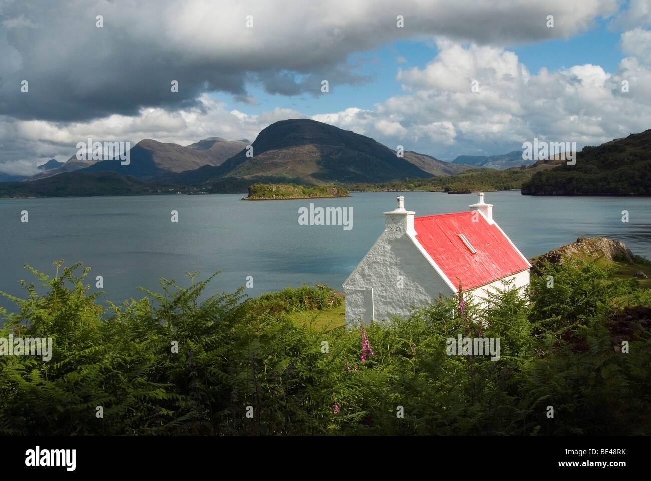 Il Croft di piccole dimensioni con un tetto rosso sul Loch Shieldaig con Ben Shieldaig, Beinn Damh nella distanza. Foto Stock