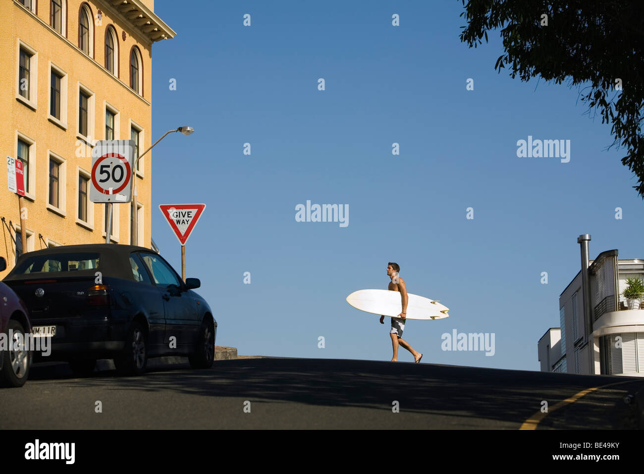 Uomo che porta la tavola da surf lungo la strada a Bondi Beach. Sydney, Nuovo Galles del Sud, Australia Foto Stock