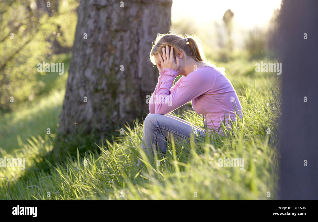 Junge Frau sitzt im Gras zwischen Baeumen Foto Stock