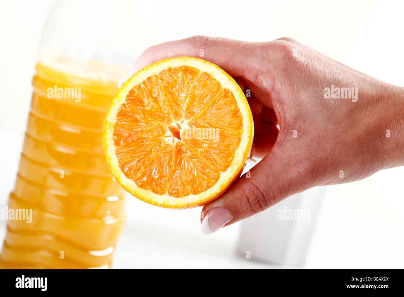 Mano che tiene la metà di un arancione nella parte anteriore di una bottiglia di succo di arancia Foto Stock