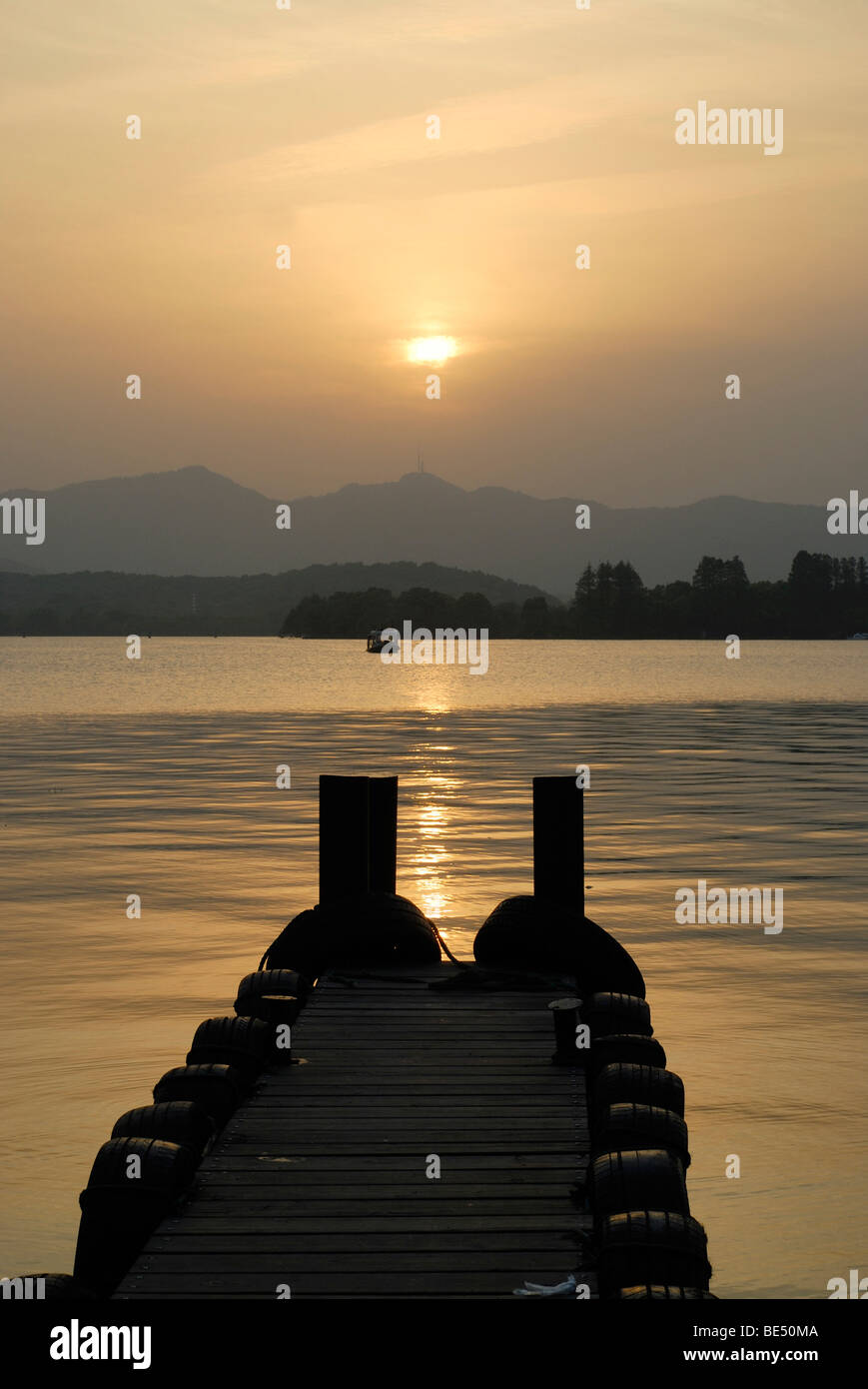 Sole di sera con una passerella di legno al lago Occidentale, Cinese: Xi Hu, di fronte a uno sfondo montano e barca, Hangzhou, Cina, Foto Stock