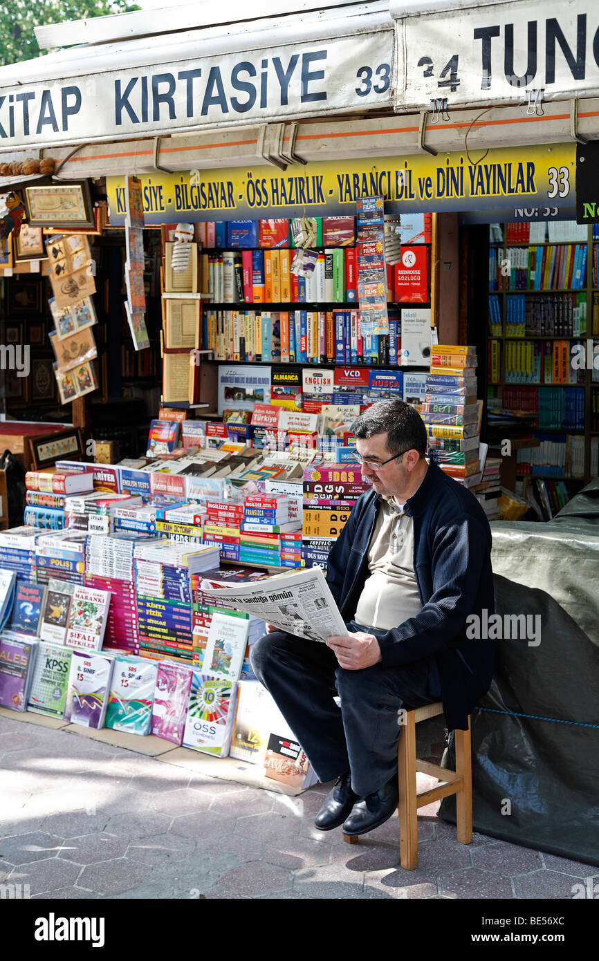 Libraio si siede davanti al suo stallo, la lettura dei giornali e prenota bazaar, Beyazit Square, Istanbul, Turchia Foto Stock