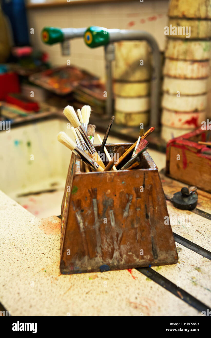 Vernice usata spazzole in un vecchio vaso di vernice con altri utilizzati materiali artistici e il lavandino come sfondo. Foto Stock