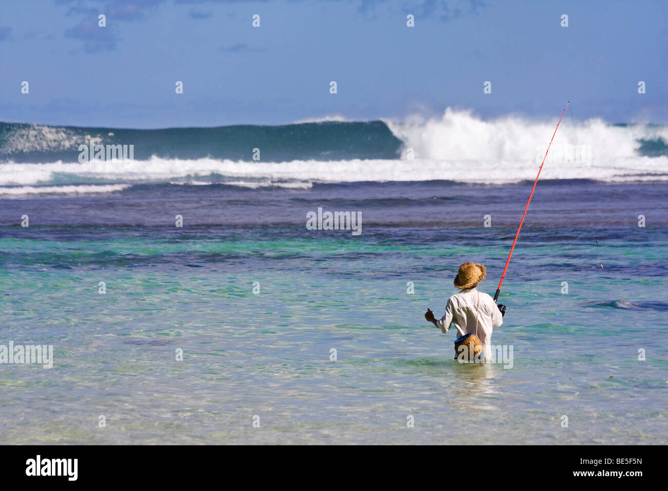 Pescatore con il tradizionale design Balinese hat la pesca al riparo dalla barriera corallina con grandi onde che si infrangono in background. Bali, Indonesia Foto Stock