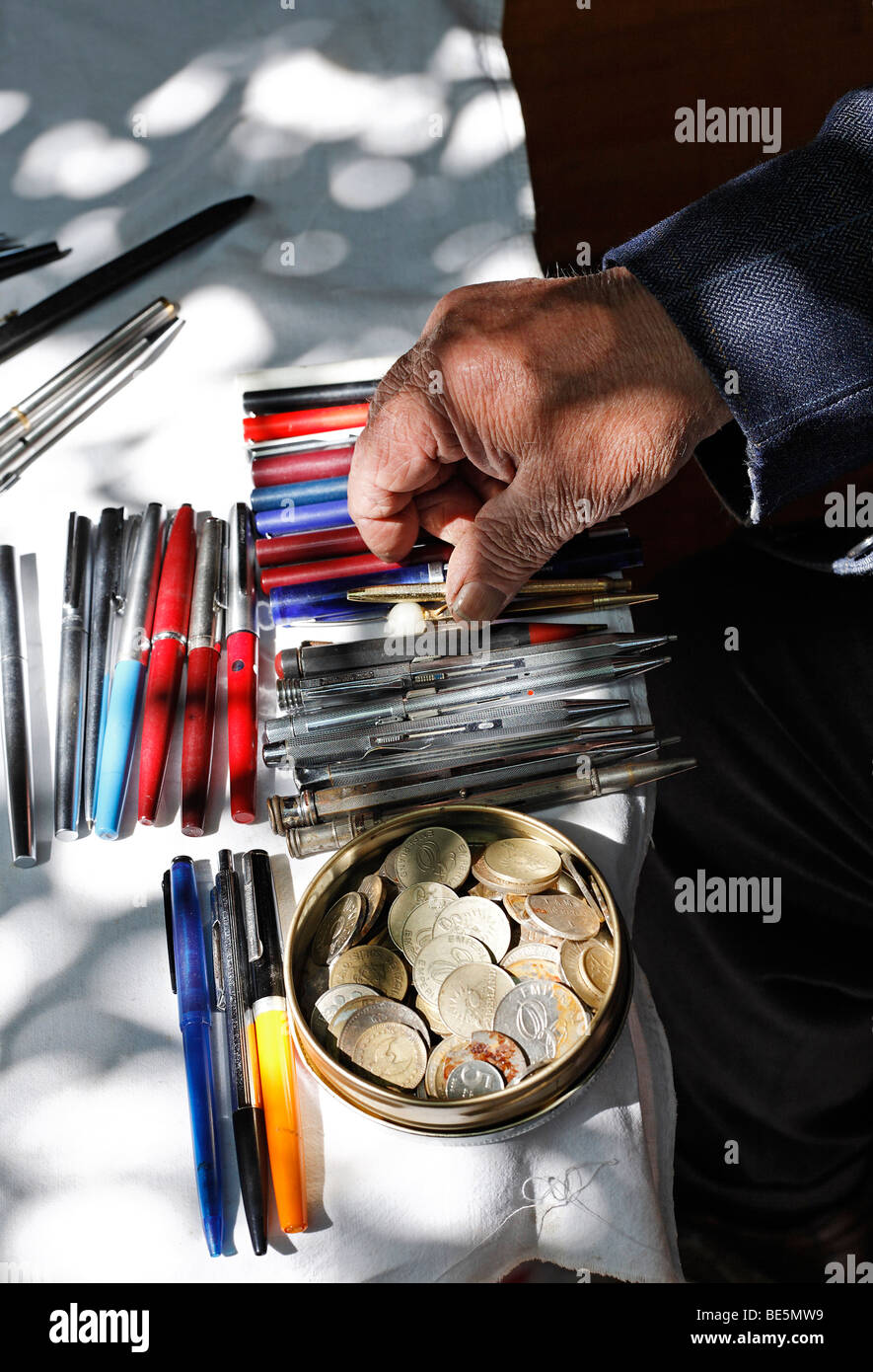 La mano di un uomo vecchio di smistamento utilizzato biros su un tavolo, monete in barattolo di latta, prenota bazaar, Beyazit Square, Istanbul, Turchia Foto Stock