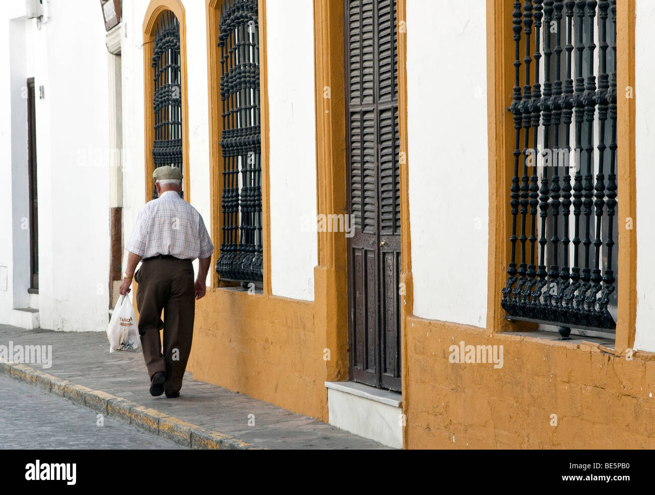 Senior uomo spagnolo sta camminando sul marciapiede con un sacchetto della spesa in mano nel villaggio andaluso di Vejer de la Frontera Foto Stock