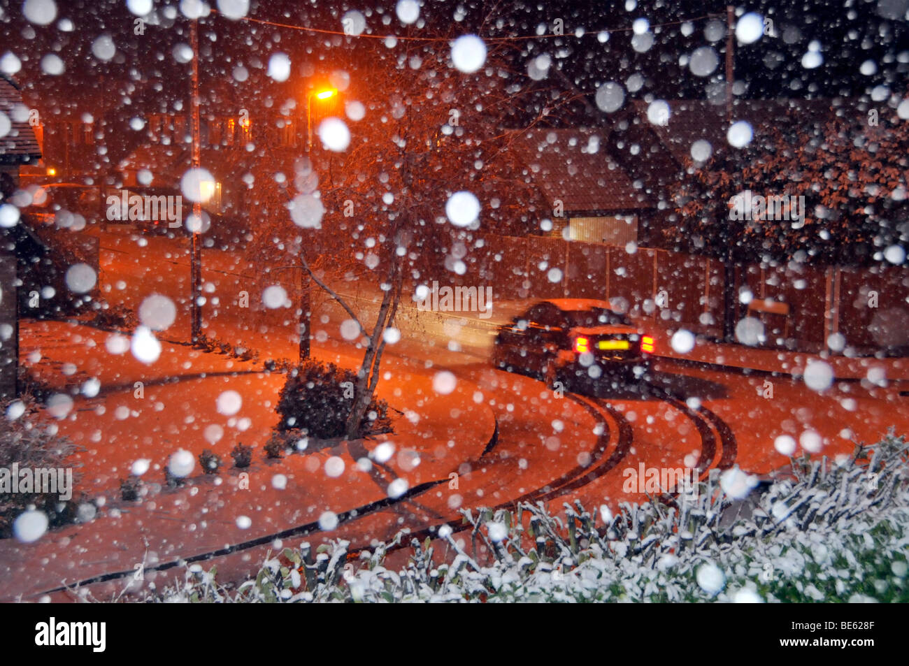 Fiocchi di neve da flash con illuminazione arancio illuminazione di strade coperte di neve strada residenziale paesaggio auto guidando lungo la strada Foto Stock