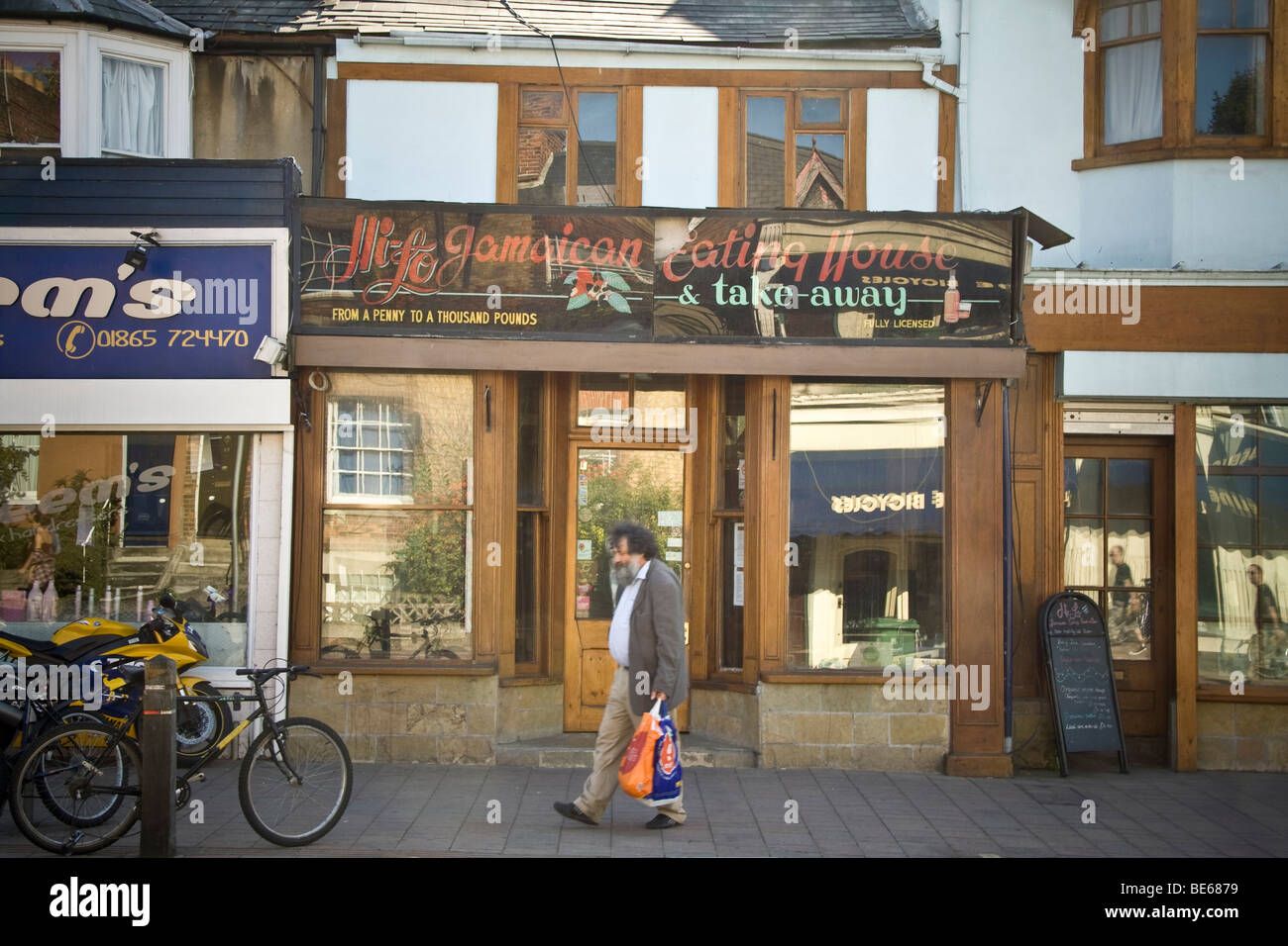 Un uomo a camminare lungo la hi lo mangia giamaicano casa ristorante bar e prendere via cowley road oxford REGNO UNITO Foto Stock