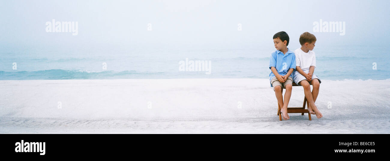 Due ragazzi seduti fianco a fianco su sedia pieghevole a beach ignorando un altro Foto Stock
