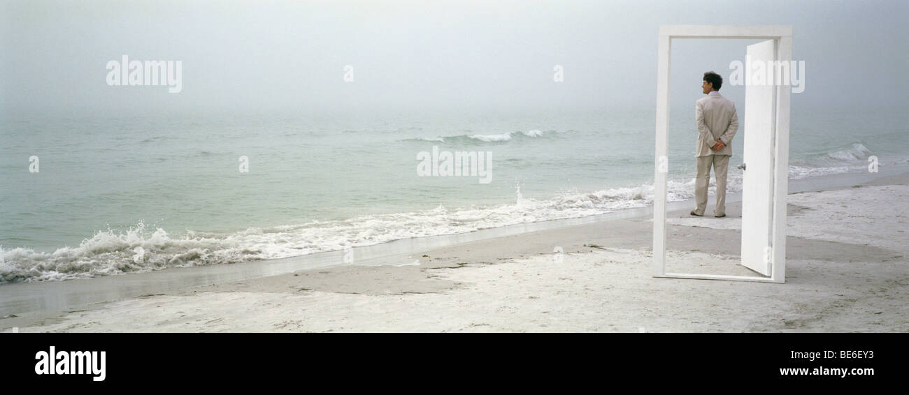 Uomo sulla spiaggia ammirando vista, visto attraverso la porta aperta Foto Stock