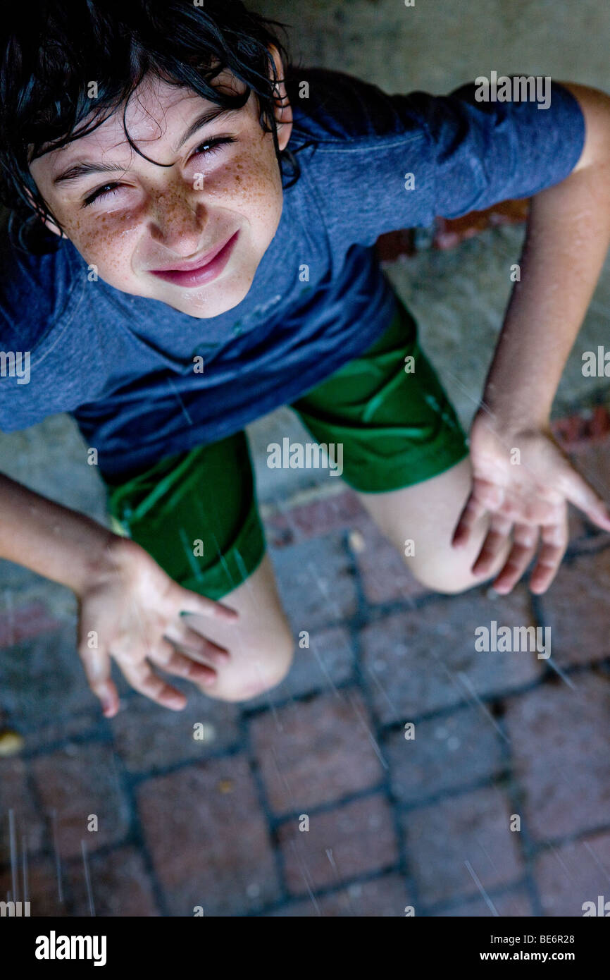 Ragazzo giovane si siede sul portico anteriore passi sotto la pioggia tenendo le mani aperte di sky Foto Stock