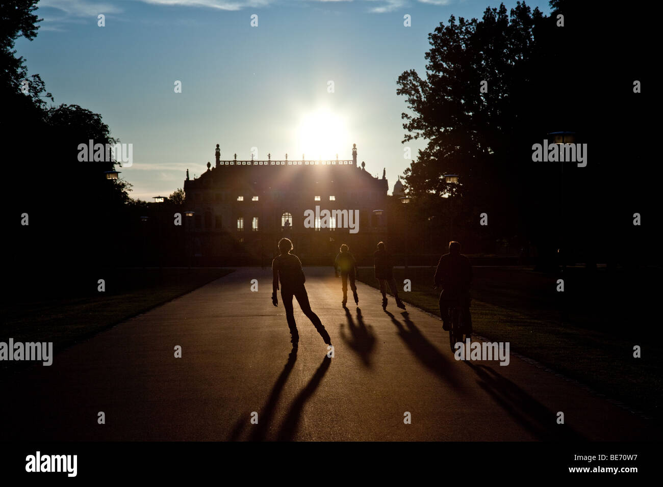 Sagome di alcuni pattinatori del rullo nella parte anteriore del palazzo in Grosser Garten park a Dresda, in Germania, durante il tramonto Foto Stock
