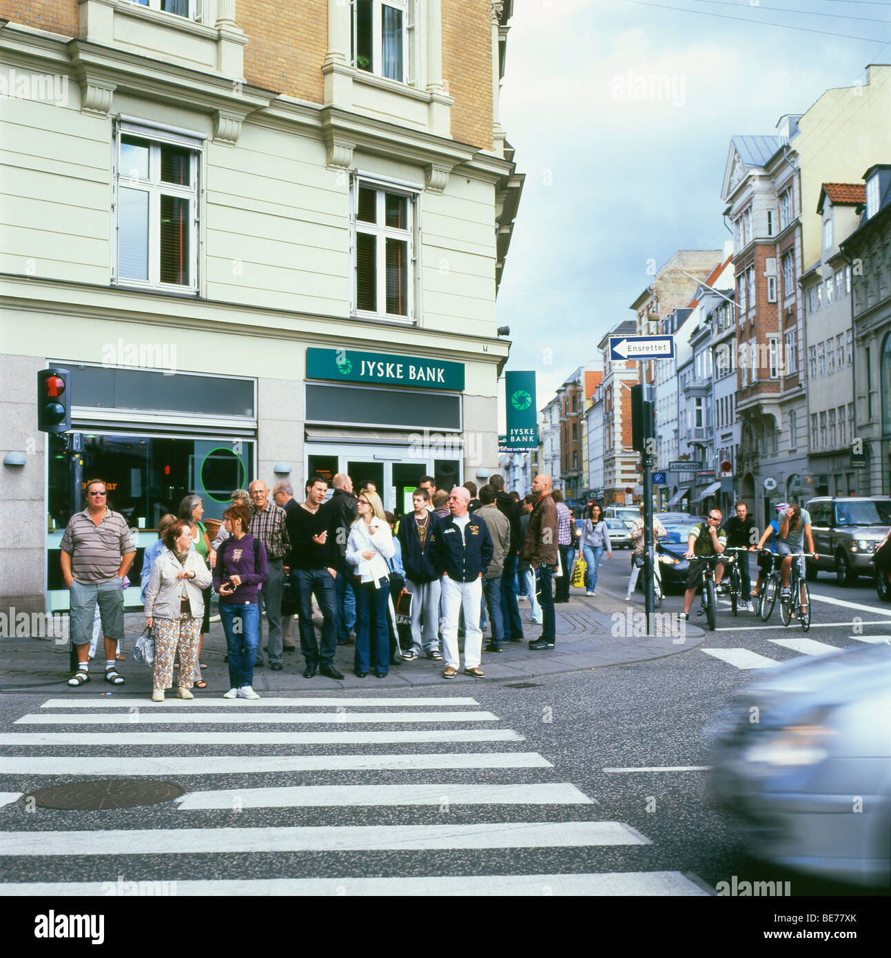 I pedoni e i ciclisti in attesa ad un semaforo e strisce pedonali nei pressi di un Jyske Bank in una strada in Copenhagen DANIMARCA Foto Stock