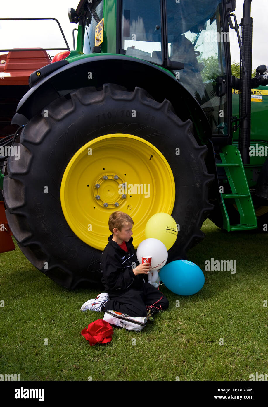 Ragazzo con palloncini Sat Coke potabile vicino a un trattore in un paese mostrano Foto Stock